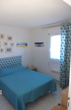 A bedroom with a bed, a nightstand, a window with curtains, and wall art.