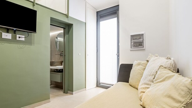 Una habitación con cama, televisión, baño y puerta que da a un balcón.