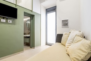 A room with a bed, a television, a bathroom, and a door leading to a balcony.