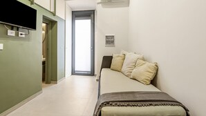 Un dormitorio con cama, almohadas, televisor, equipo de aire acondicionado y puerta que da a un balcón.