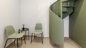 Un interior moderno con dos sillas verdes, una mesita y una escalera de caracol.