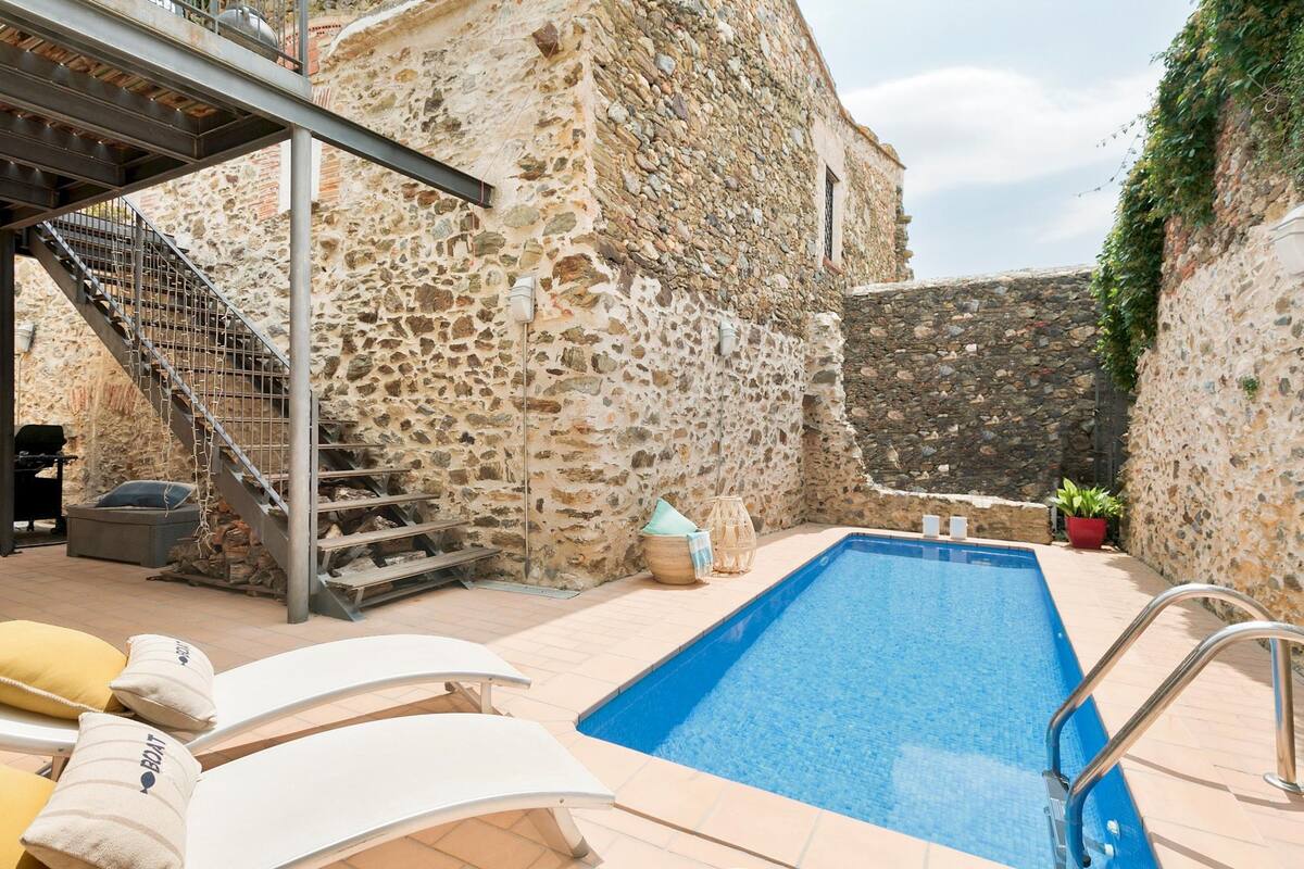 Un edificio de piedra con piscina, mobiliario exterior y una escalera.