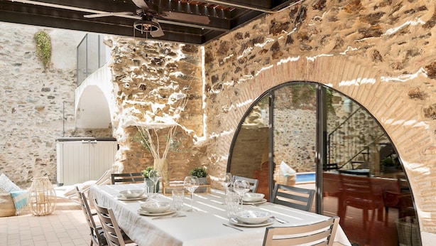 An outdoor dining area with stone walls, a table set for four, and a view of the interior through an arched doorway. - Garriguella- Roses Pool Costa Brava House (Garriguella)