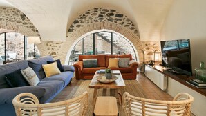 A cozy living room with a stone arch, a sofa, a coffee table, and a TV. - Garriguella- Roses Pool Costa Brava House (Garriguella)