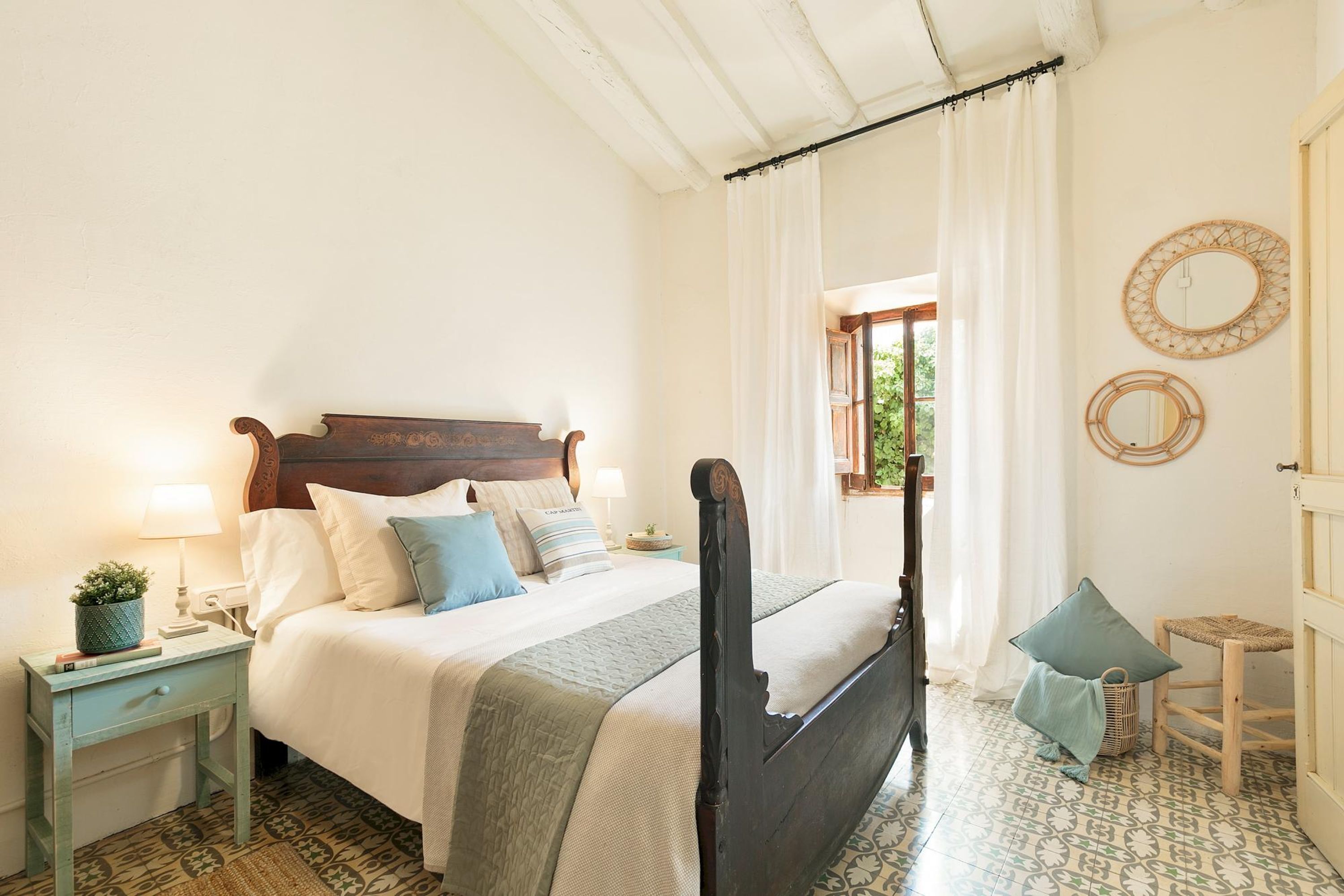 A neatly arranged bedroom with a bed, bedside tables, a small chair, and a window with curtains.
