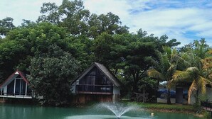 A houseboat with a water fountain, surrounded by lush greenery and trees. - The wide view resort cafe (Thep Krasattri)