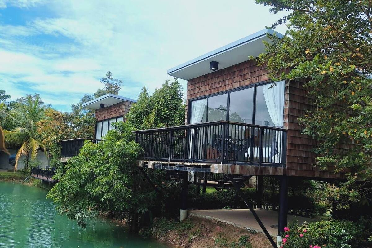 A house with a deck over a body of water, surrounded by greenery.