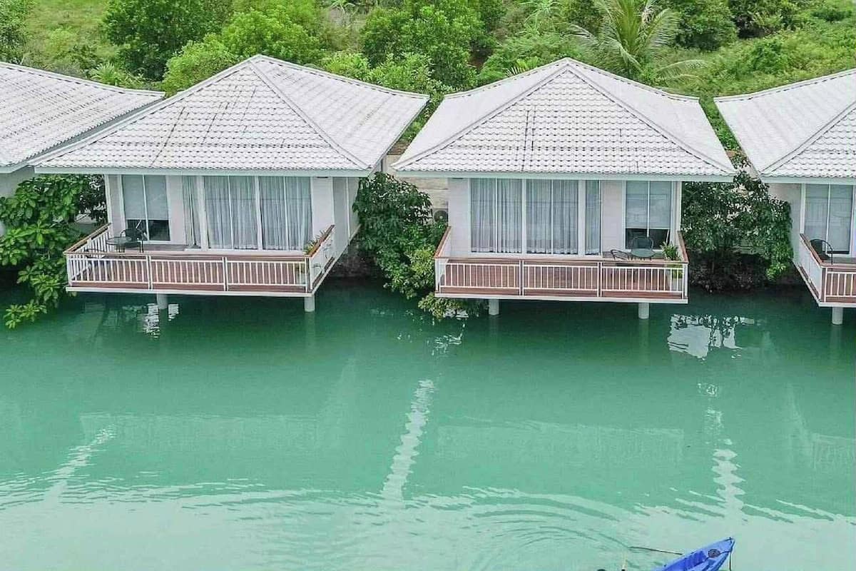 Overwater bungalows with balconies, surrounded by water and greenery.