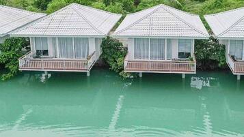 Overwater bungalows with balconies, surrounded by water and greenery.