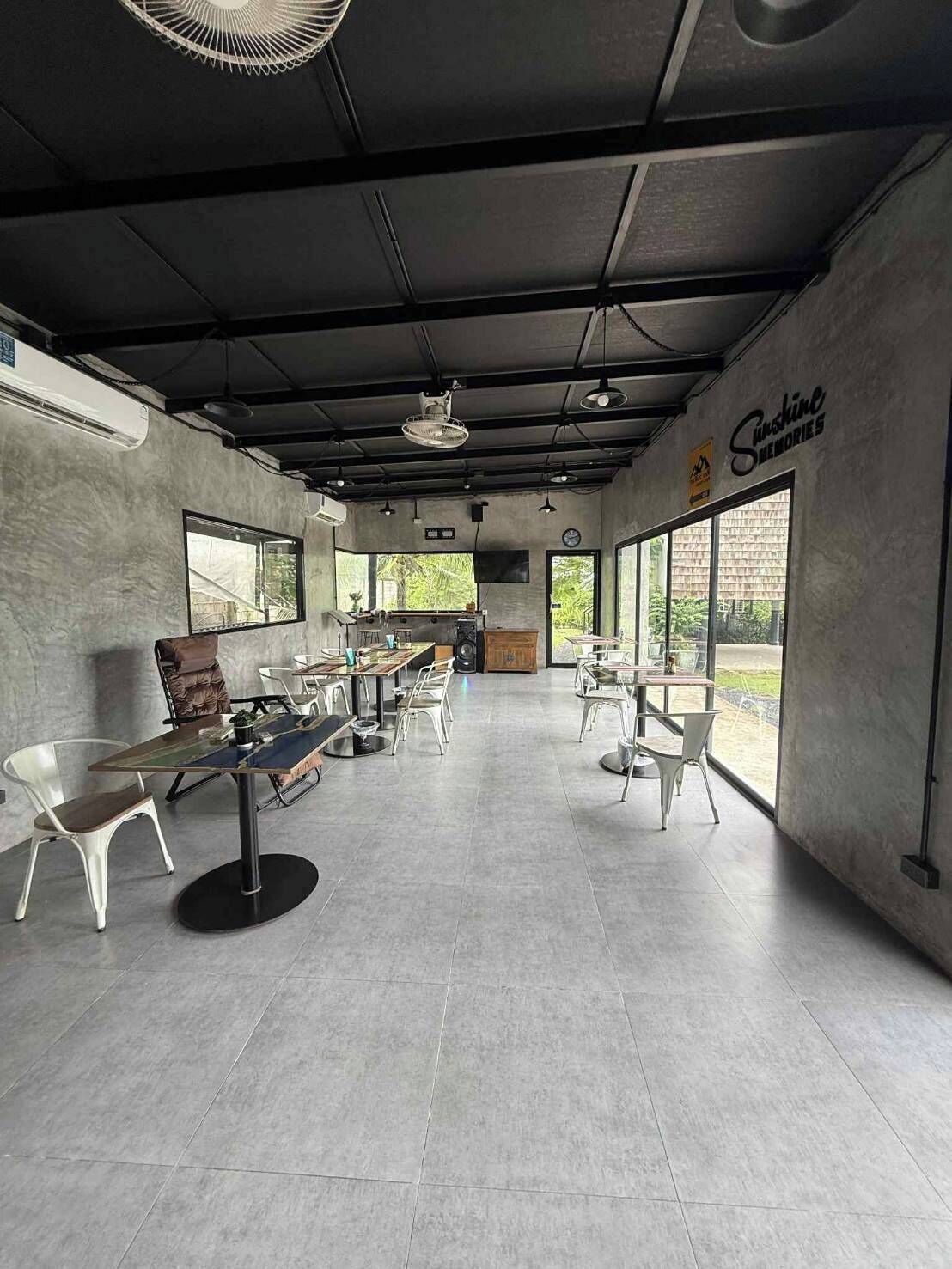 A spacious cafe with modern furniture, large windows, and a sign reading "Sunshine Memories".