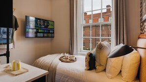 Une chambre d’hôtel avec un lit, un téléviseur fixé au mur, une fenêtre donnant sur des immeubles et un plateau avec des articles pour le petit-déjeuner posé sur le lit.