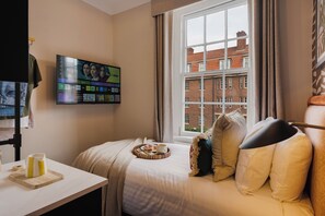 Quarto de hotel com cama, televisão fixada na parede, janela com vista para edifícios e bandeja com itens de café da manhã sobre a cama.