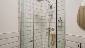 Une douche avec une porte en verre, des murs recouverts de carreaux blancs et un pommeau de douche à main.