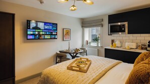 Un dormitorio moderno con cama, televisor, mesa de comedor y zona de cocina.