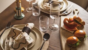 A dining table set with plates, cutlery, glasses, and a sandwich.
