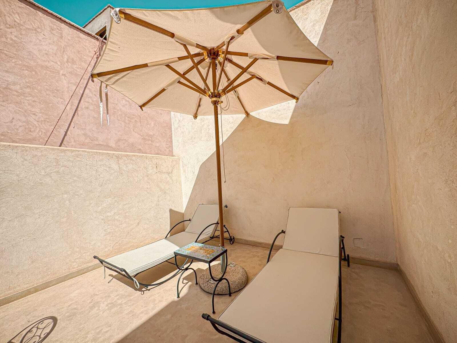 A small outdoor seating area with a table, a chair, and a large umbrella providing shade.