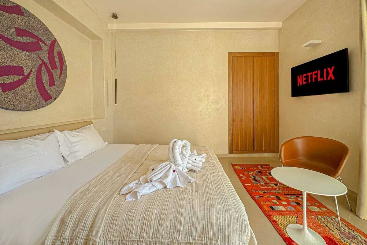 A hotel room with a bed, a TV, a wooden door, and a red patterned rug.
