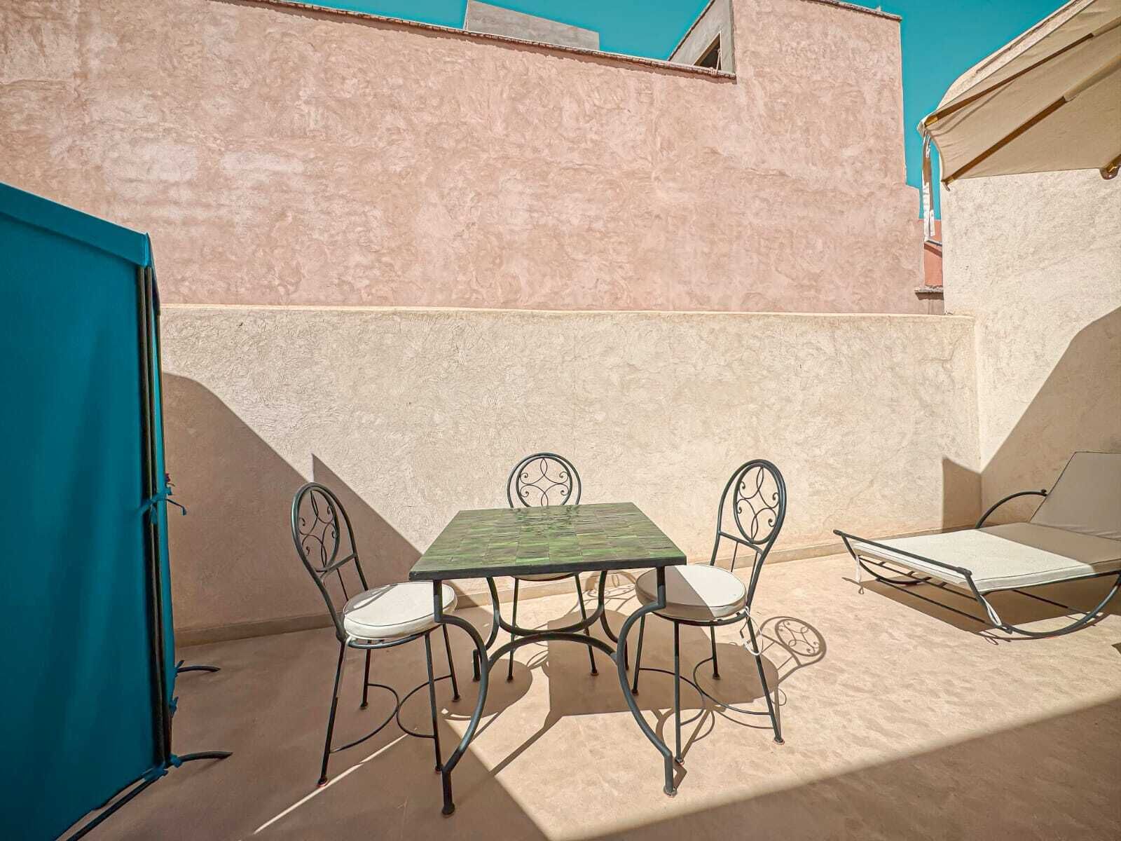 A patio with a table and four chairs, a sun lounger, and a blue door.