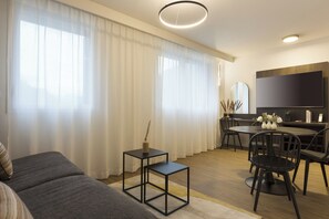 A modern living room with a sofa, a small table, and a dining area with chairs. - Nehô Suites St Jean de Maurienne (Saint-Jean-de-Maurienne)