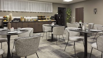 A dining area with round tables, chairs, and a buffet counter with food and beverages.