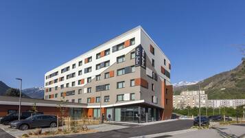 Un hôtel à plusieurs étages au design moderne, caractérisé par une façade aux couleurs contrastées, allant du blanc au gris, et une enseigne bien visible indiquant « Michele Suites ».