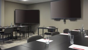 A conference room with a large screen, tables, chairs, and water bottles.