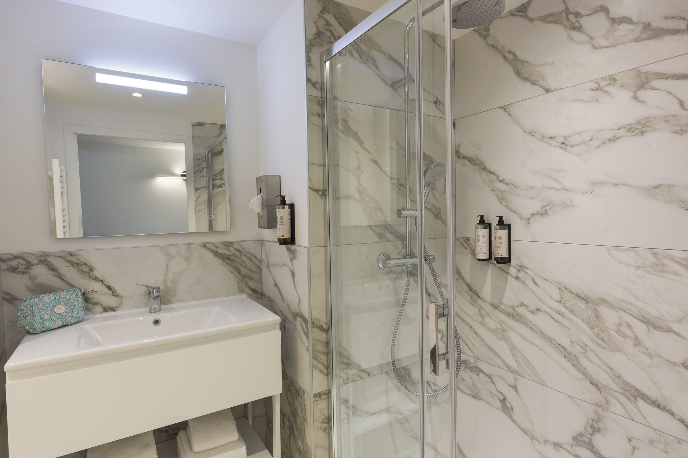A bathroom with a glass-enclosed shower, a white sink, and a marble-tiled wall.