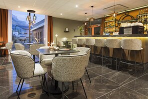 A bar area with a bar counter, seating with chairs, and a view of the outside. - Nehô Suites St Jean de Maurienne (Saint-Jean-de-Maurienne)