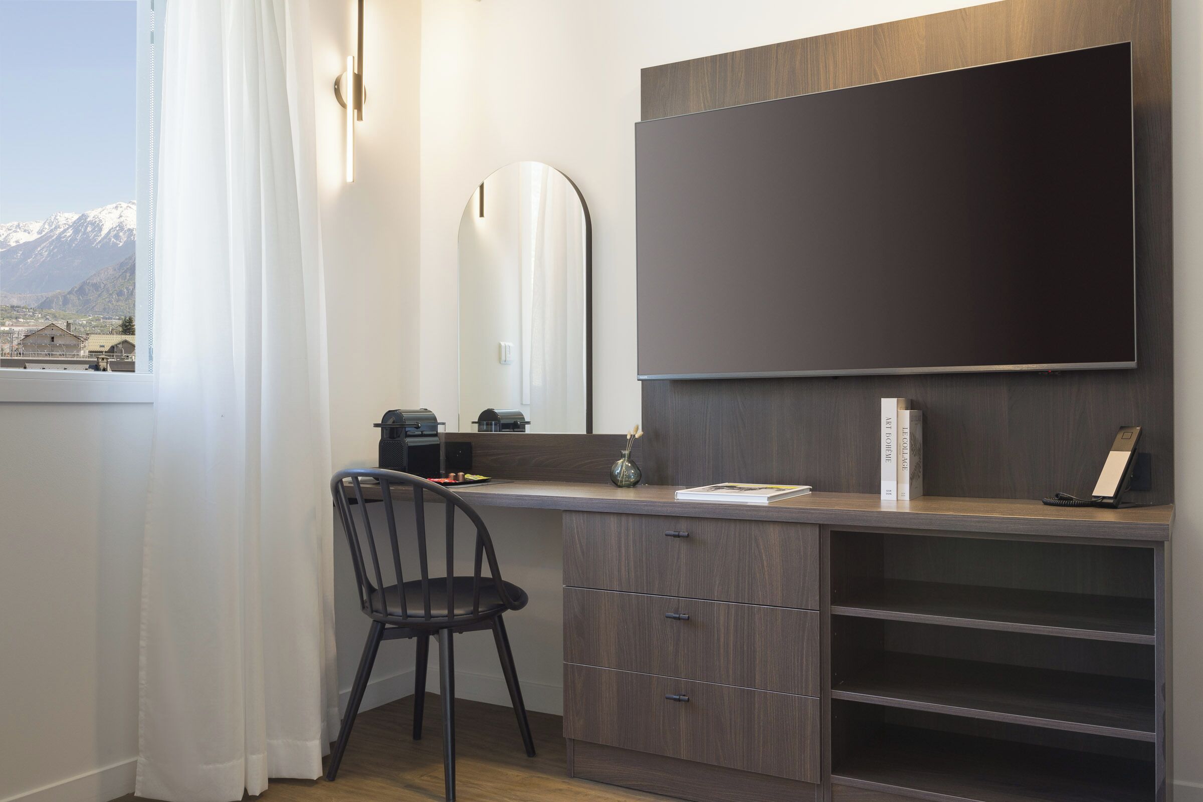 Une chambre moderne dotée d’une grande fenêtre, d’un bureau avec une chaise, d’un téléviseur à écran plat et d’une bibliothèque.