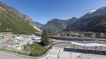 Un paisaje montañoso con una estación de tren, un puente peatonal y un aparcamiento.