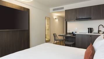 A hotel room with a bed, a desk, a chair, a flat-screen TV, and a kitchenette.