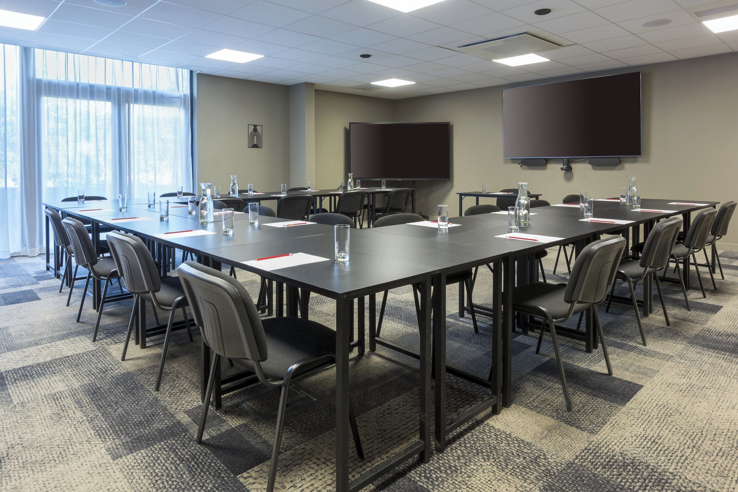 A conference room with a long table, chairs, a projector screen, and a large window with curtains.