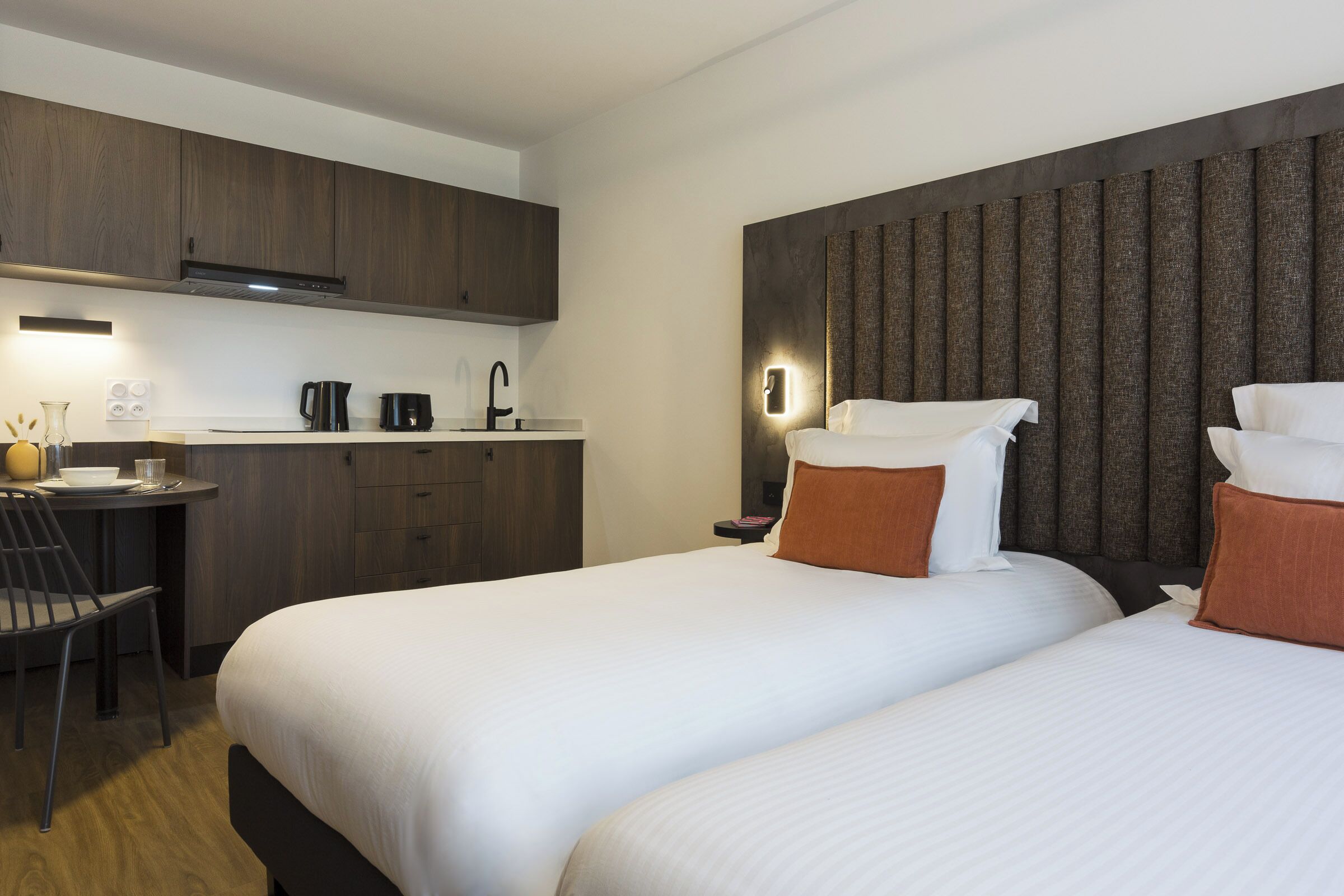 A hotel room with two beds, a kitchenette, a dining area, and a bathroom.