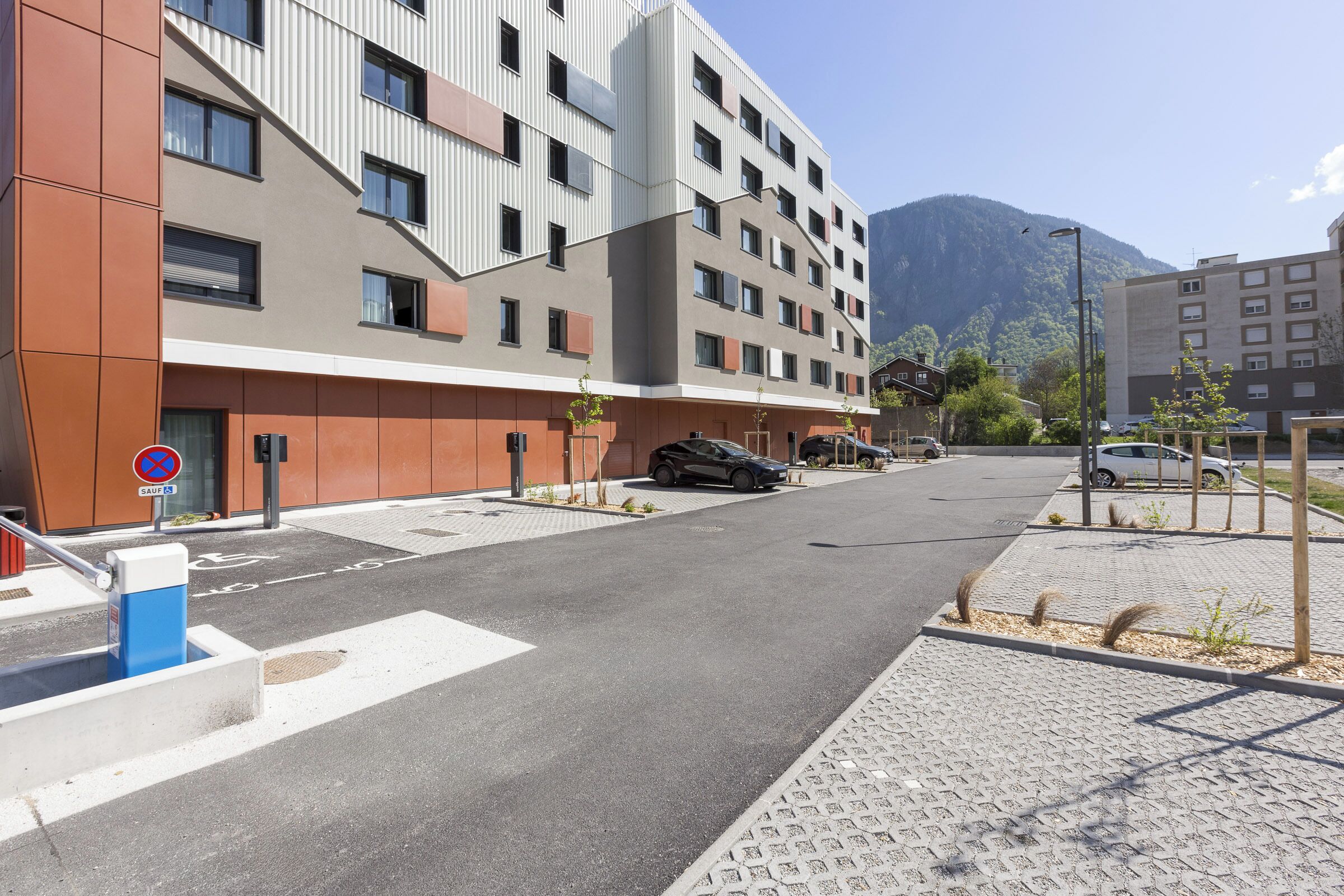 A modern building with a flat roof, multiple windows, and a parking area in front.
