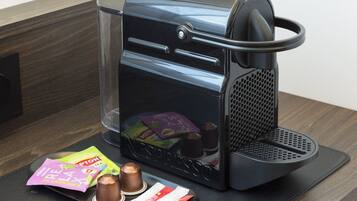 A coffee machine with a clear water reservoir, a coffee pod holder, and a few coffee pods and chocolate cups on the counter.