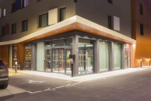 A modern hotel entrance with a glass door entrance, a wheelchair-accessible ramp, and a parking area. - Nehô Suites St Jean de Maurienne (Saint-Jean-de-Maurienne)