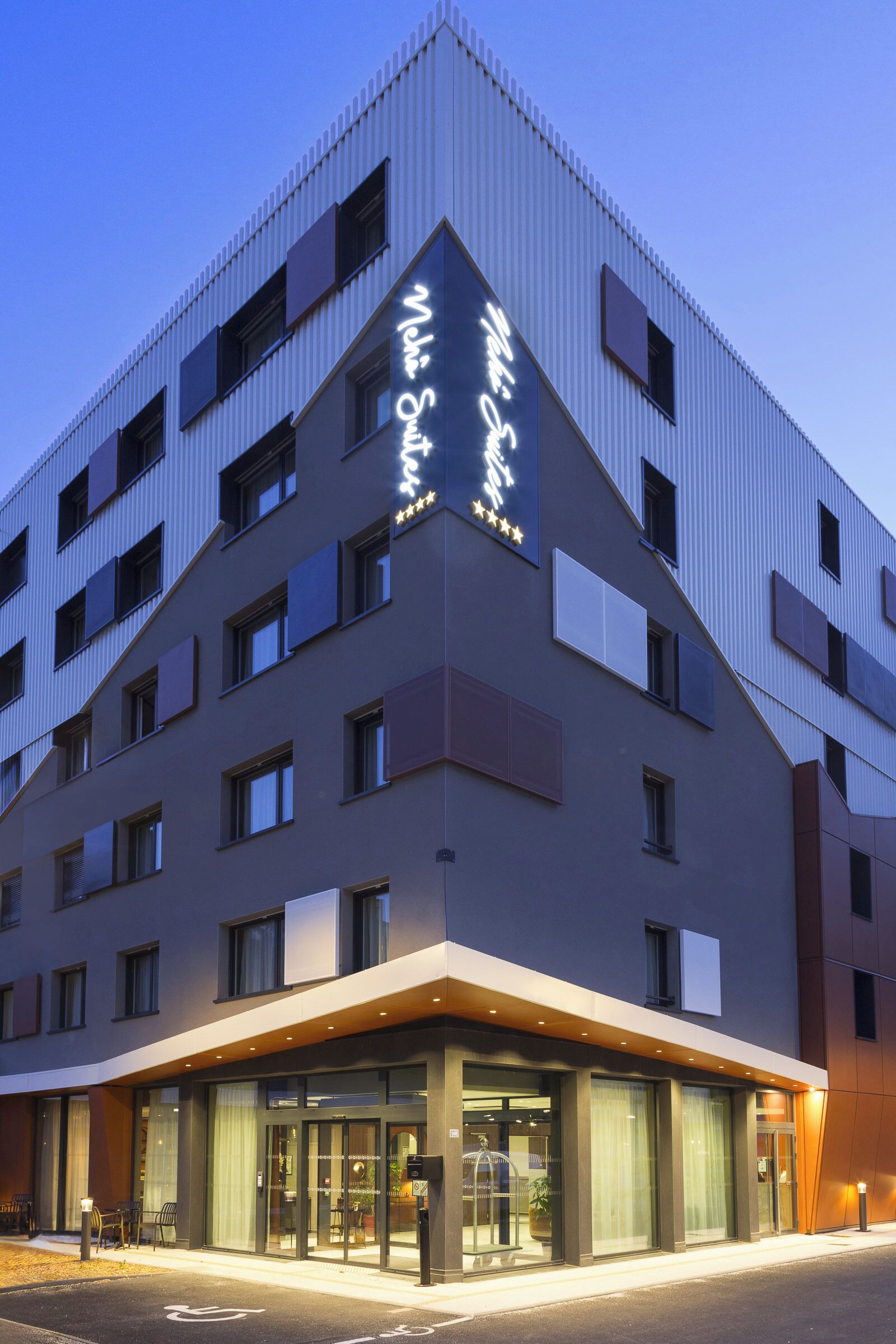 Een modern hotelgebouw met een opvallend bord, grote ramen en een goed verlichte entree.
