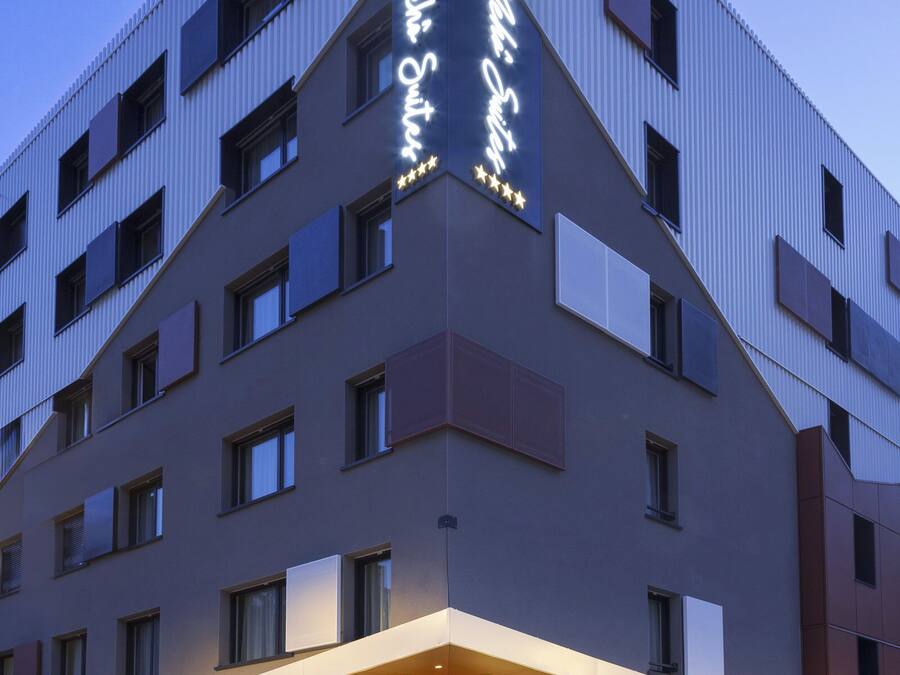 A modern hotel building with a prominent sign, large windows, and a well-lit entrance.