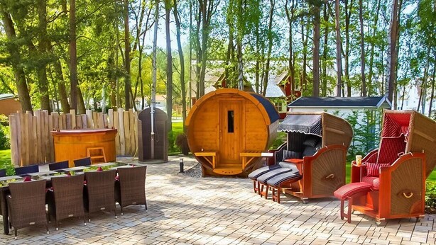 Ein Außenbereich mit Sitzgelegenheiten, einem Holzfass, Korbstühlen und einem roten Stuhl.