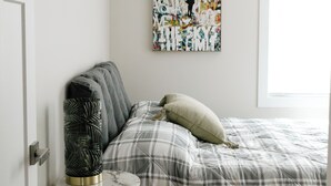 Een slaapkamer met een bed, een nachtkastje, een kunstwerk aan de muur en een deur.