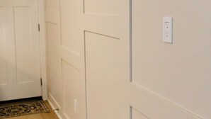 Een hal met houten vloer, witte wanden met panelen, een deur en een lichtschakelaar.