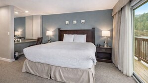 A hotel room with a large bed, a desk, two chairs, a nightstand, and a window with curtains. - Bayside Waterfront King_Ocean Views_King Bed_Pool (Eastsound)