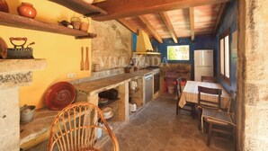 Une cuisine rustique avec des poutres en bois, des murs en pierre et un coin repas comprenant une table et des chaises.