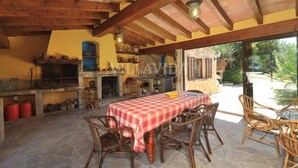 Une cuisine extérieure avec une nappe à carreaux, des chaises en osier et un sol en pierre.