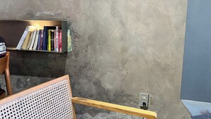 Espaço de leitura com estante, uma cadeira e tomada em parede texturizada.