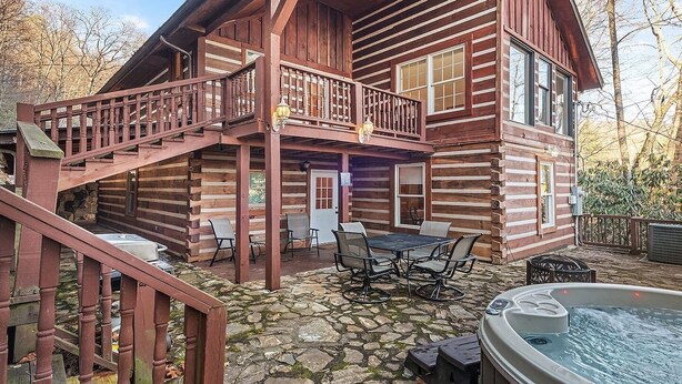 Una cabaña de troncos con un patio de piedra, mobiliario exterior y un jacuzzi.