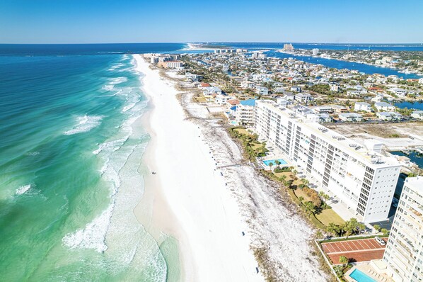 An aerial view of a coastal city with a beachfront hotel, featuring a long sandy beach, ocean views, and dense urban development.