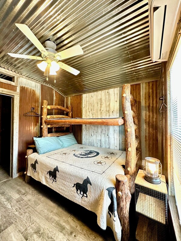 A rustic bedroom with a bed, wooden headboard, and a ceiling fan.