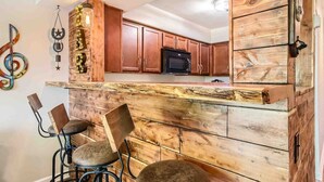 A kitchen with wooden cabinets, a microwave, and a bar area with stools. - Music City Living - 2BR/2BA Riverfront Paradise with FREE PARKING (Nashville)