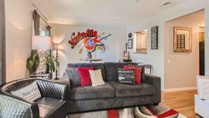 A living room with a grey sofa, two armchairs, a lamp, and a wall mural of Nashville.